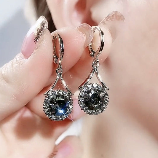 Silver earrings with blue gemstones held between fingers against a blurred background