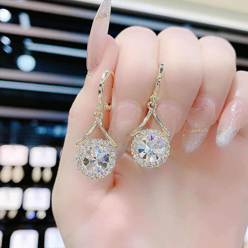 Gold earrings with large gemstones held between fingers against a blurred background