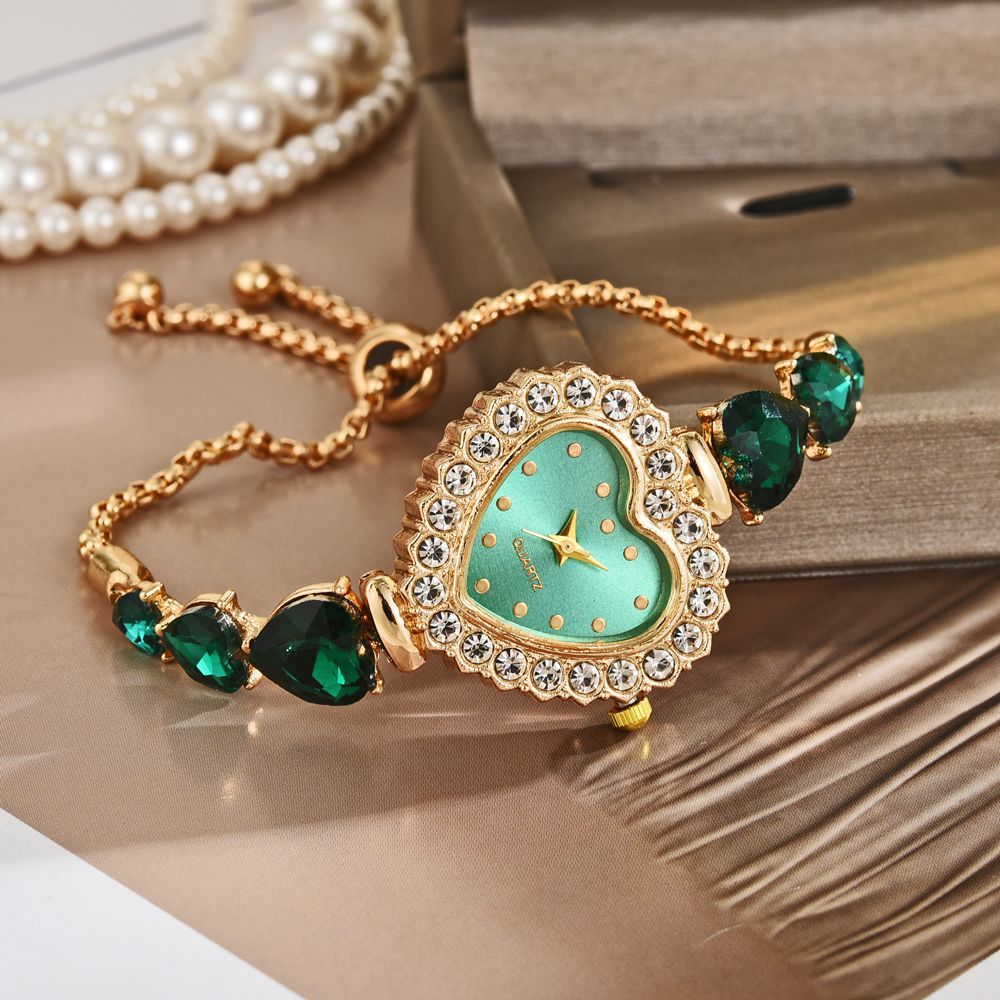 Heart-shaped quartz wrist watch with green stones and gold strap on a stylish background.