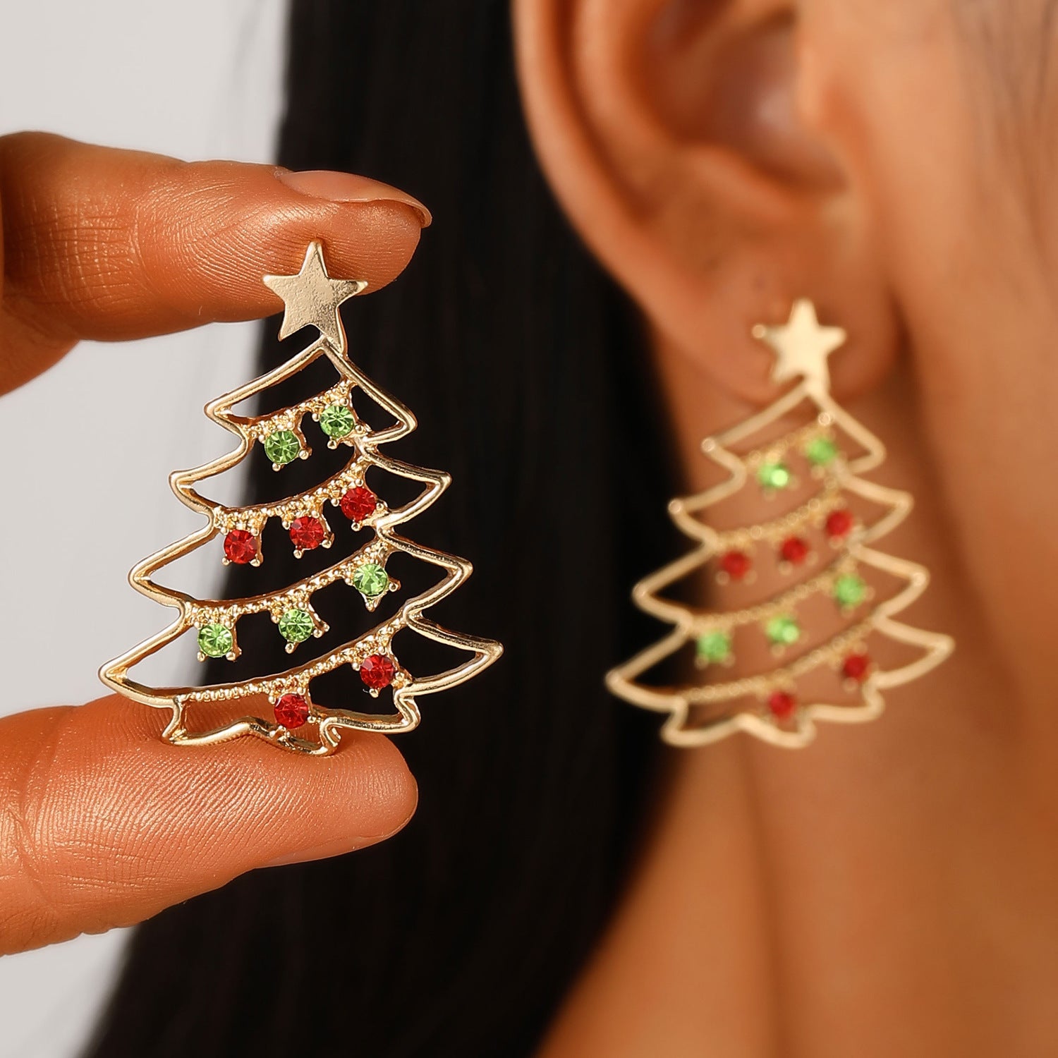 Christmas tree-shaped earrings with red and green accents held near an ear.